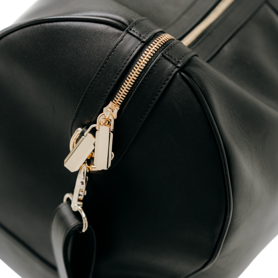 Close up view of the side of the black premium leather bag with gold zipper and handle hook