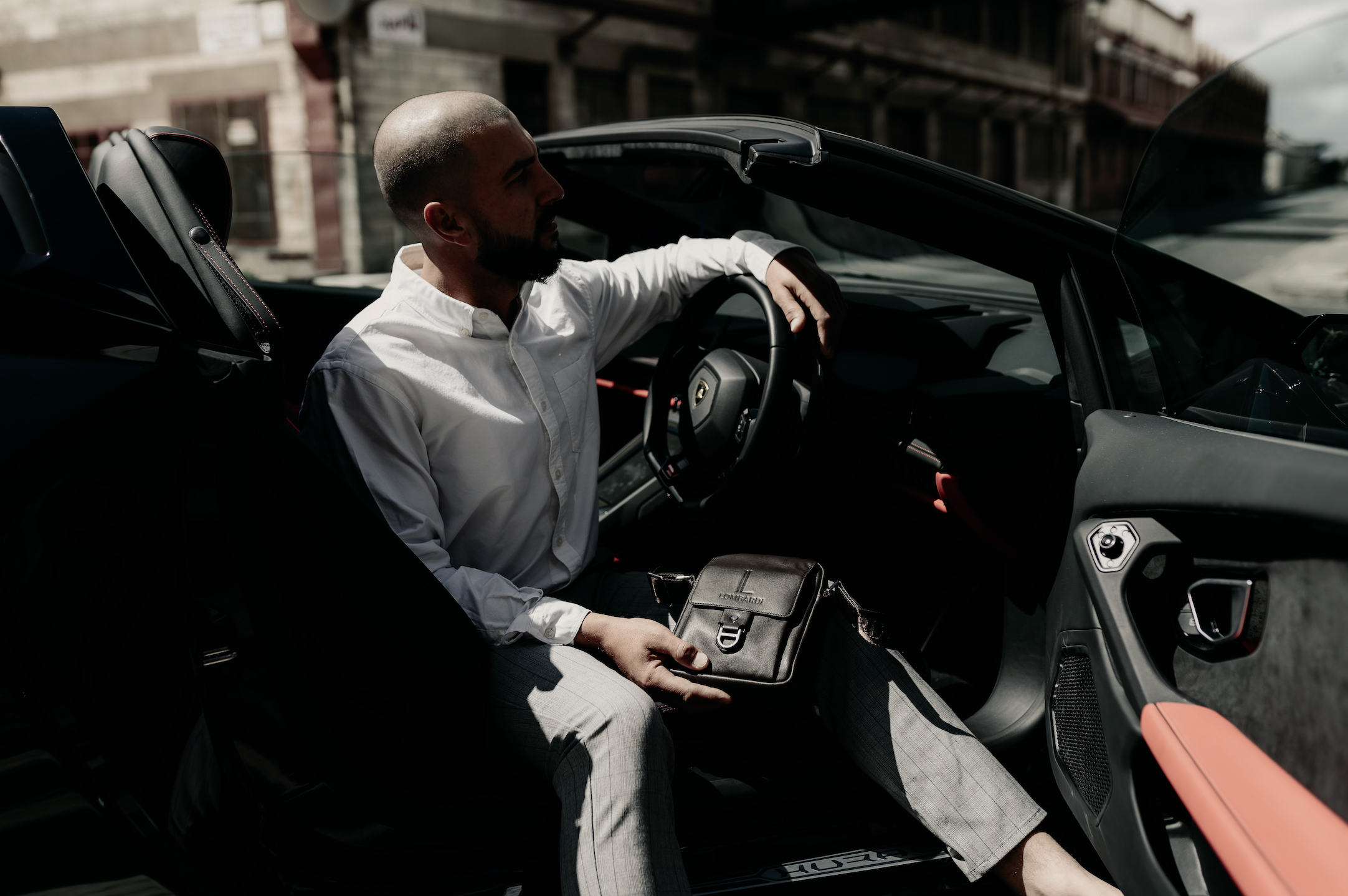 Stylish man getting out of a Lamborghini with the black leather classic edition satchel